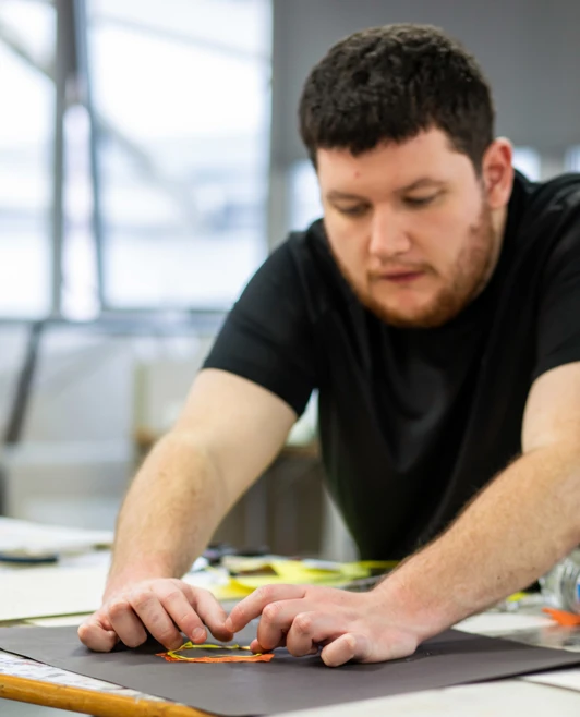 Student in a black shirt focusing on a hands-on art project, using both hands to arrange materials on a black surface Student in a black shirt focusing on a hands-on art project, using both hands to arrange materials on a black surface